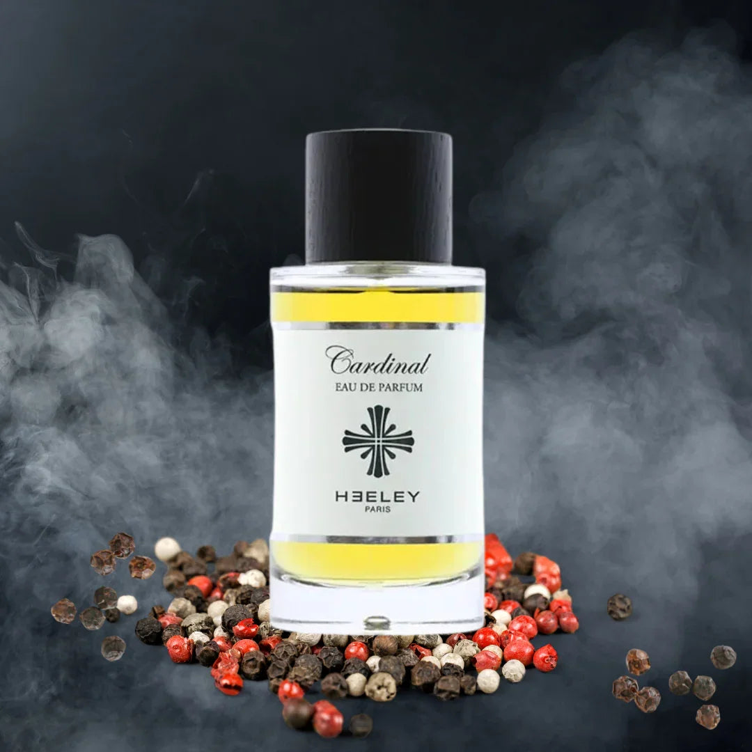 Transparenter 100ml-Flakon "Cardinal" von Heeley, gefüllt mit gelblicher Flüssigkeit und schwarzem Deckel, umgeben von Pfefferkörnern.