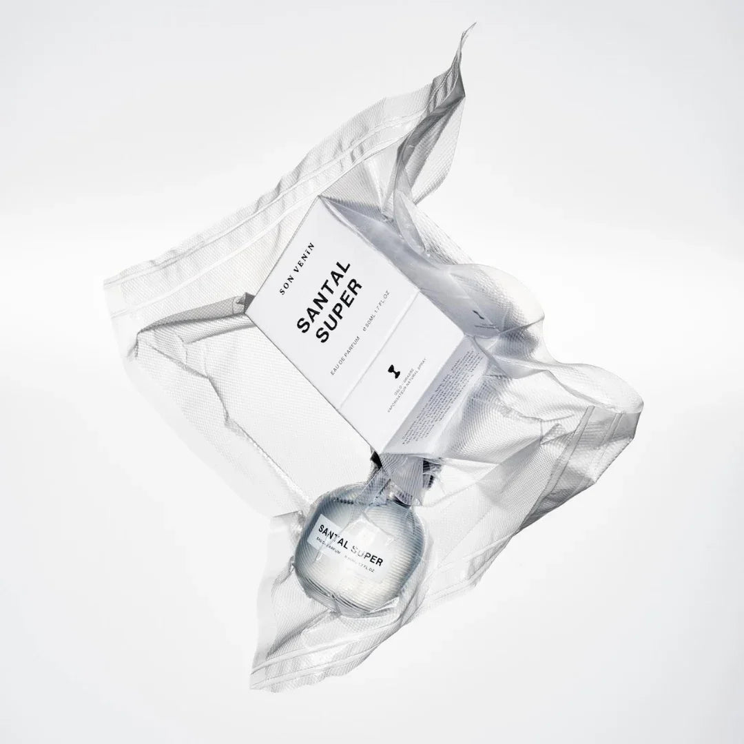 Das Produkt "Santal Super" von SON VENÏN ist eine Flasche Parfüm, verpackt in einem transparenten, strukturierten Kunststoff. Auf der Verpackung steht der Produktname und der Markenname.