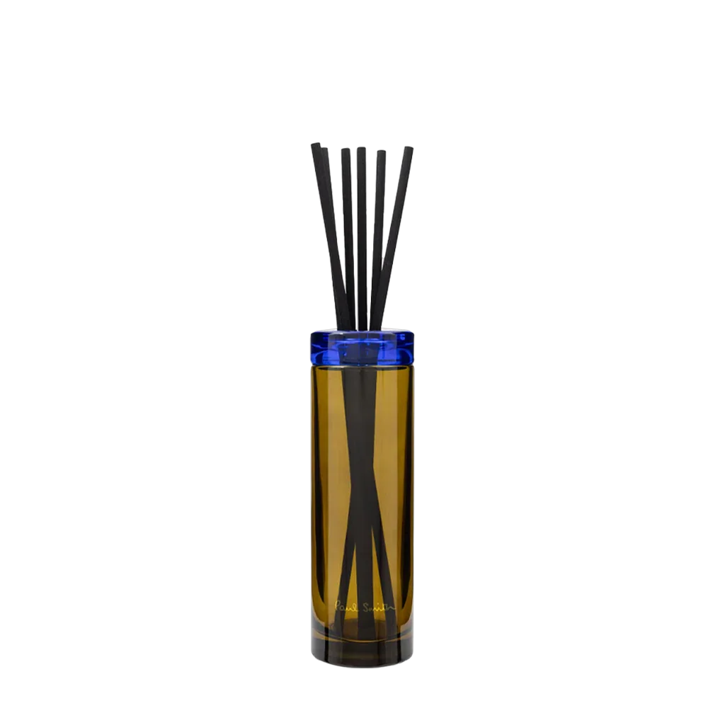 Ein zylinderförmiger Diffusor mit goldener Glasoberfläche und blauem Randdeckel von Paul Smith. Produkt: Storyteller Diffuser.