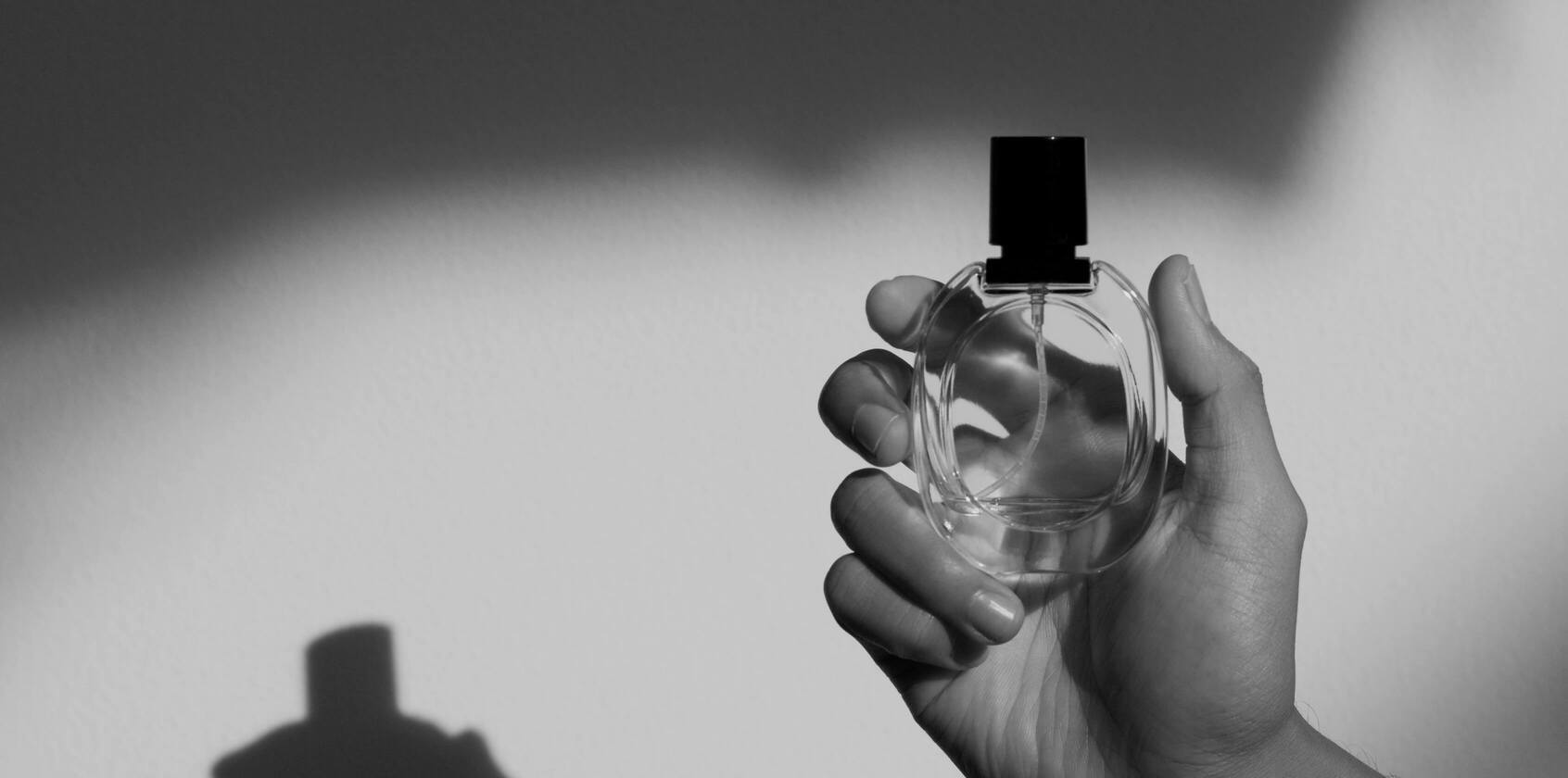 Ein transparenter Parfumflakon der vor einer weißen Wand in der Hand gehalten wird.