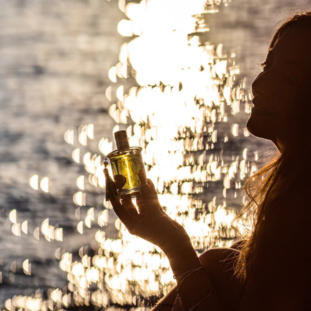 Parfums MDCI für sinnliche Sommerabende mit Motiv Frau am Meer hält Nischenduft Flakon von Parfums MDCI in der Hand