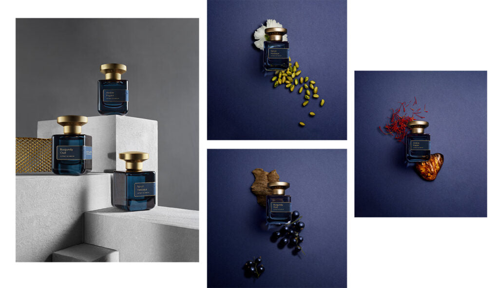 Vier blaue Parfümflaschen mit goldenen Kappen, auf Blöcken ausgestellt und mit verschiedenen Gewürzen und pflanzlichen Stoffen.