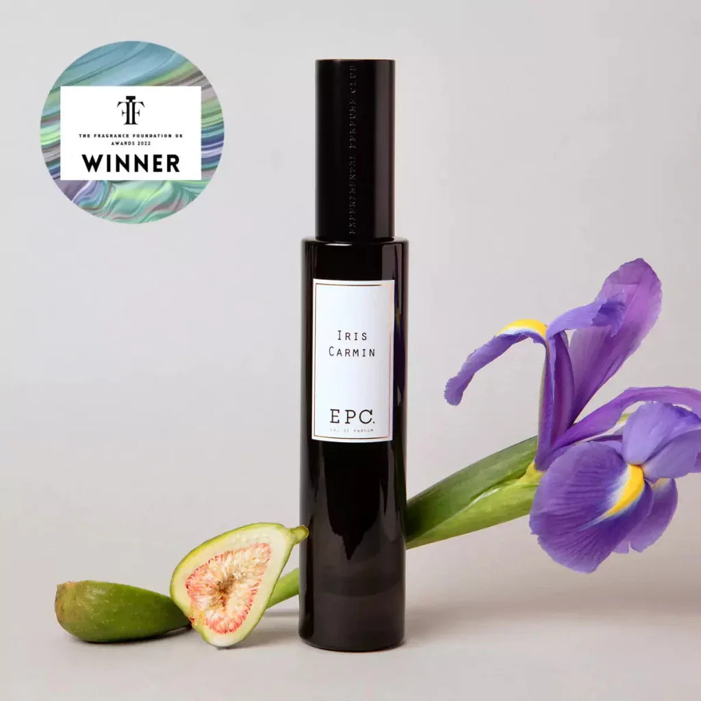 Parfümflakon "Iris Carmin" von Experimental Perfume Club neben einer lila Irisblüte und einer geschnittenen Feige bei scent amor