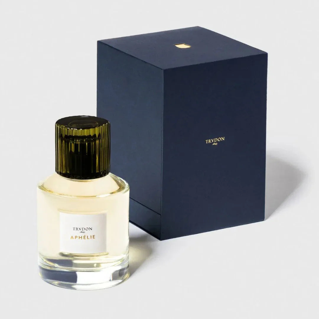 Parfümflasche "APHÉLIE" von Trudon mit cremefarbigem Etikett und schwarzem Verschluss, neben einer dunkelblauen Box präsentiert beim Fachmann für Nischenduft scent amor