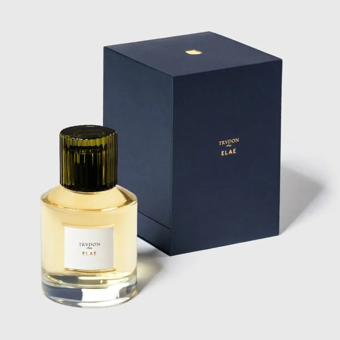 Parfümflasche mit gelber Flüssigkeit und dunklem geriffelten Verschluss, daneben eine dunkelblaue Box. Produkt: ELAE, Hersteller: Trudon bei scent amor