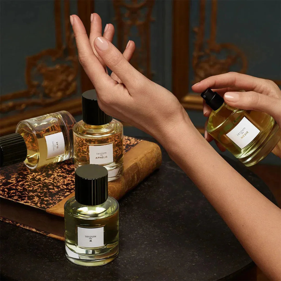 Vier Flakons II-Parfüm von Trudon, zwei auf einem Tisch, zwei gehalten von Händen, mit schwarzem Deckel. Präsentiert bei scent amor deinem Fachmann für Nischenduft.