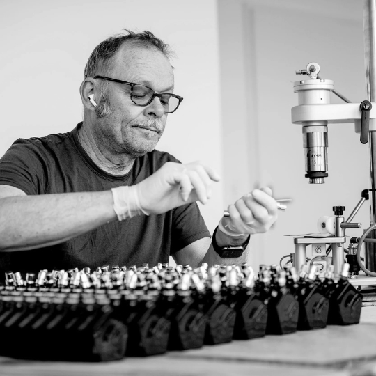 Andy Tauer in einer Schwarz-Weiß-Aufnahme bei der Arbeit im Parfum-Atelier, umgeben von Duftflakons und Präzisionswerkzeug der Parfumherstellung, erhältlich bei scent amor.