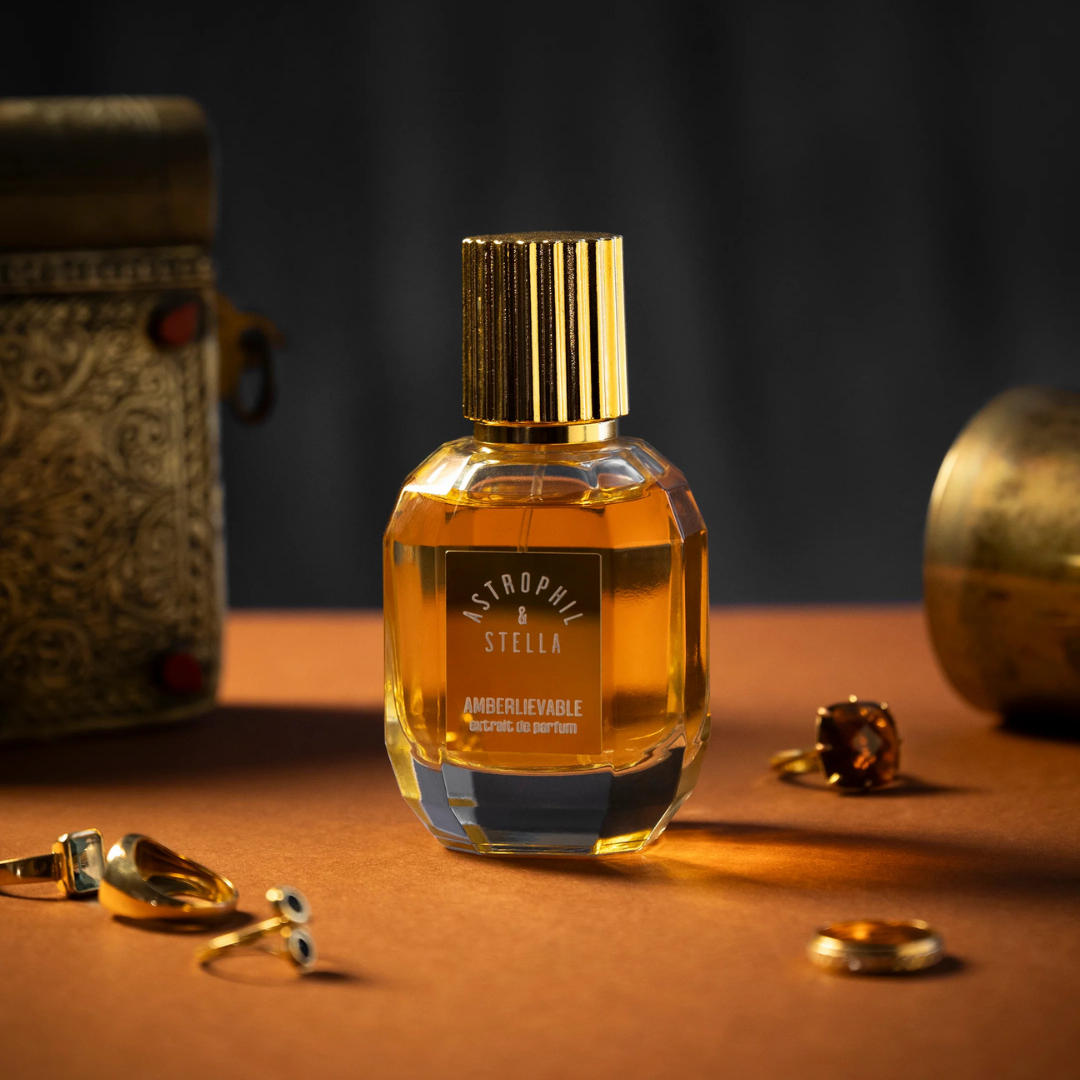 Astrophil & Stella AMBERLIEVABLE Eau de Parfum, warm leuchtender Amberduft im facettierten Glasflakon mit goldener Kappe, stilllebenartige Inszenierung mit Schmuck und orientalischer Atmosphäre, erhältlich bei scent amor.