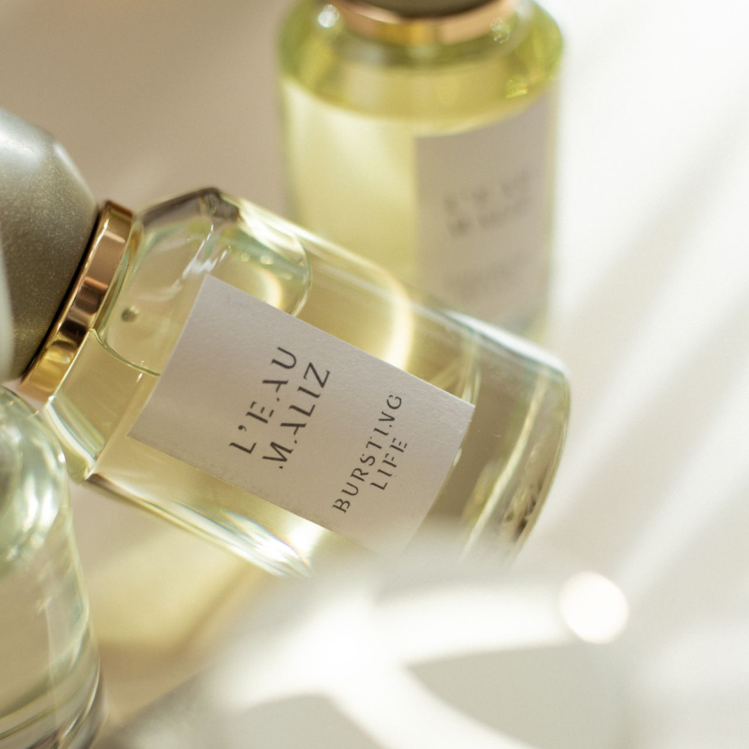 L’Eau Maliz Bursting Life Eau de Parfum, Glasflakon im warmen Licht mit sanften Reflexionen, elegant und fein, erhältlich bei scent amor.