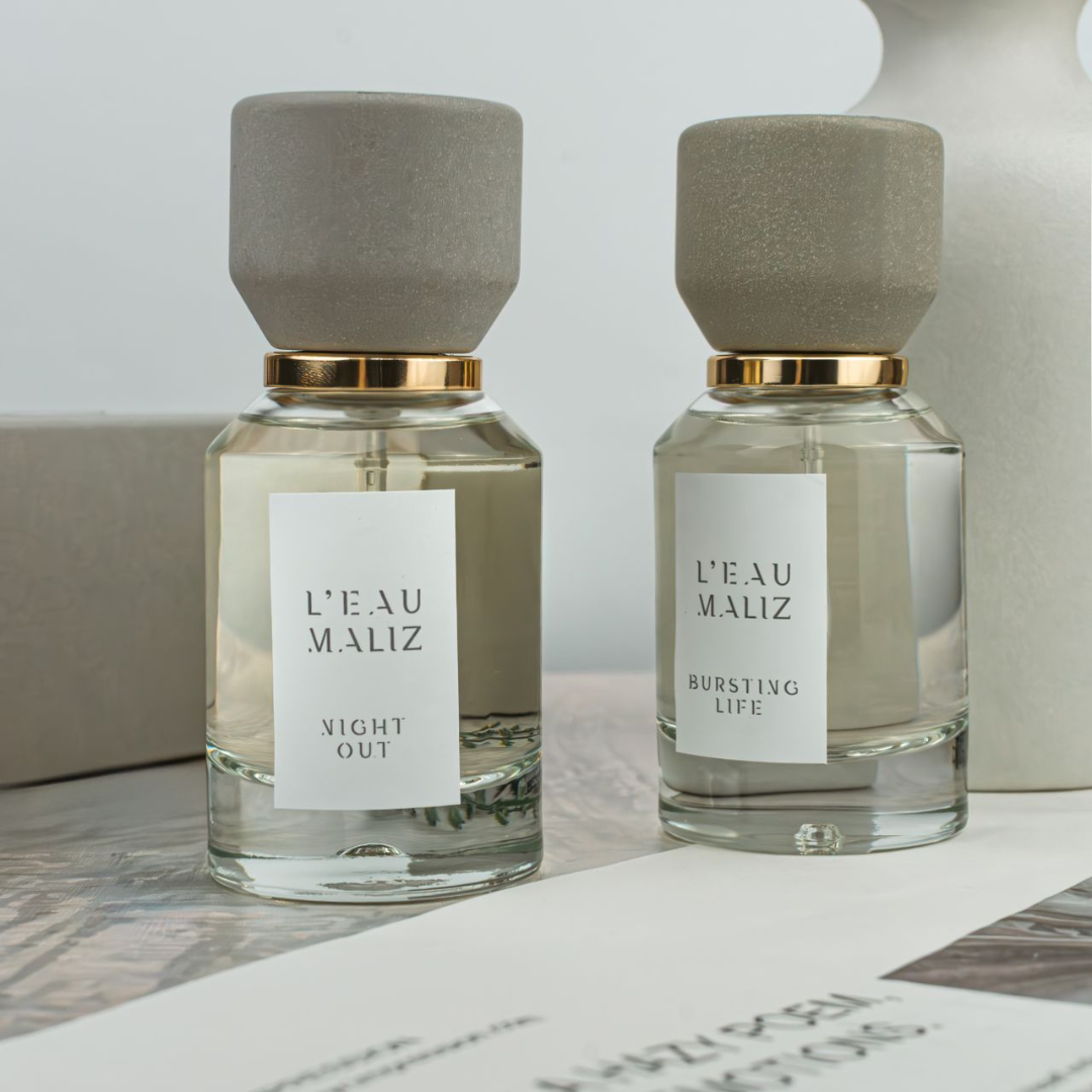 L’Eau Maliz Bursting Life Eau de Parfum, zwei Flakons in ruhiger Szene arrangiert, harmonisch und modern, erhältlich bei scent amor.