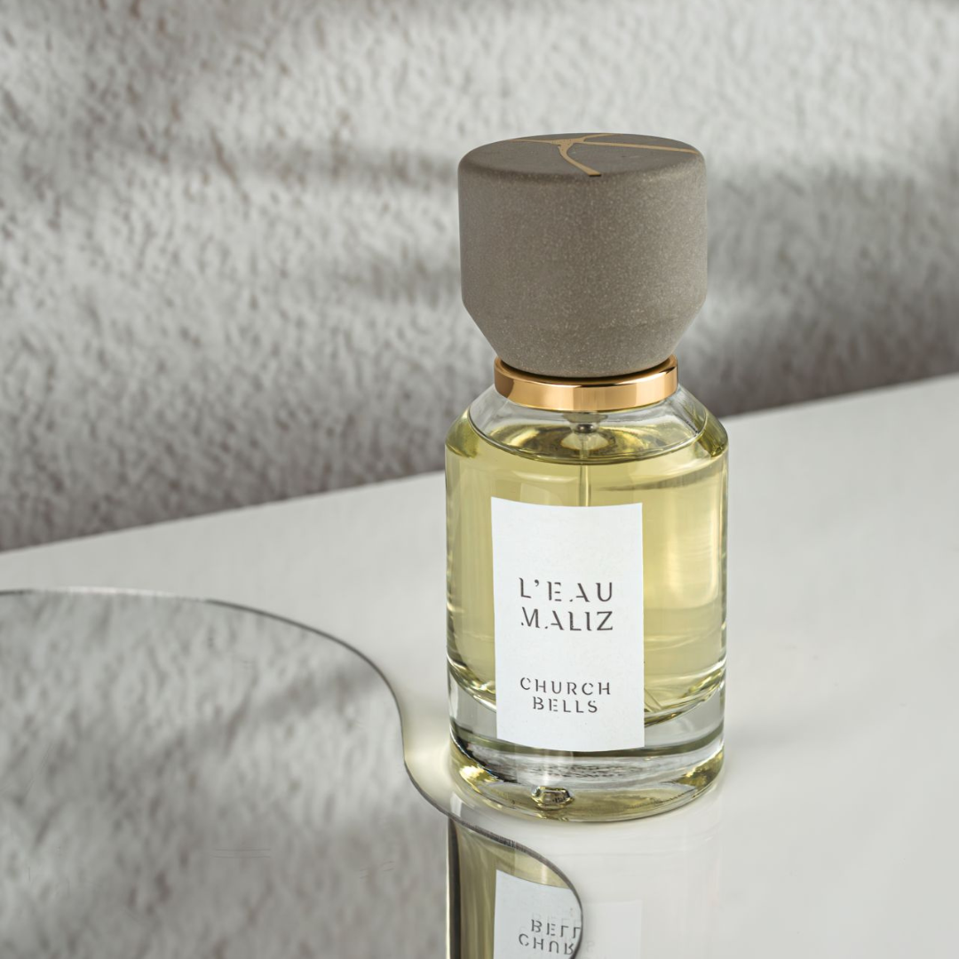 L’Eau Maliz Church Bells Eau de Parfum, Flakon auf reflektierender Oberfläche inszeniert, elegant und kontemplativ, erhältlich bei scent amor.