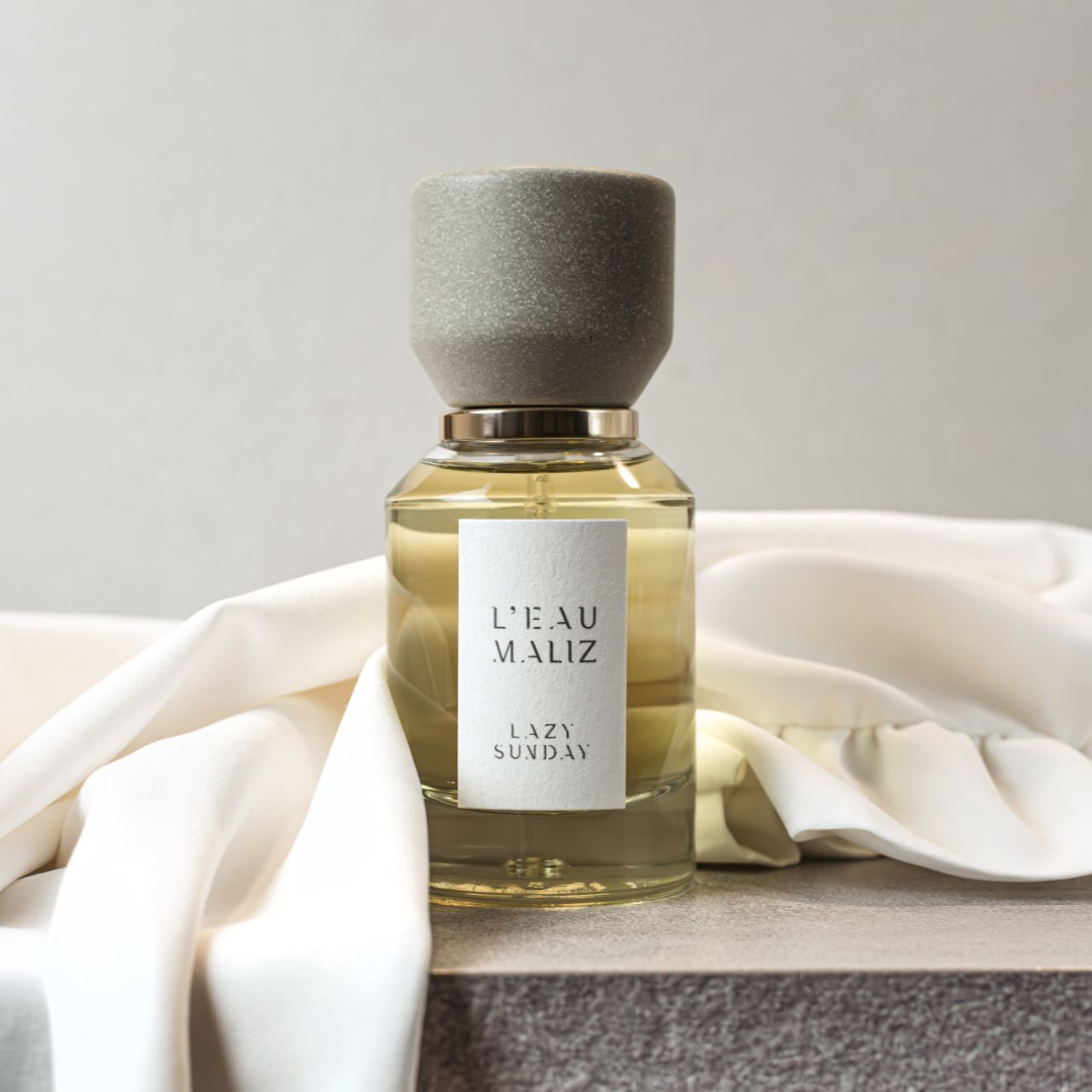 L’Eau Maliz Lazy Sunday Eau de Parfum, elegante Präsentation mit fließendem Stoff und ruhiger Farbwelt, erhältlich bei scent amor.