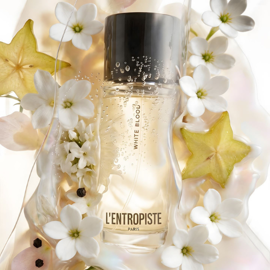L’Entropiste White Blood Eau de Parfum, Flakon umgeben von weißen Blüten, Früchten und transparenten Flüssigkeitseffekten, frische und florale Duftästhetik, erhältlich bei scent amor.
