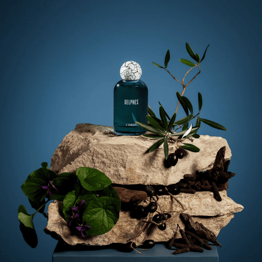 L’Objet Delphes Eau de Parfum, Flakon inszeniert auf Stein mit Olivenzweig und botanischen Elementen, mediterran und natürlich, erhältlich bei scent amor.