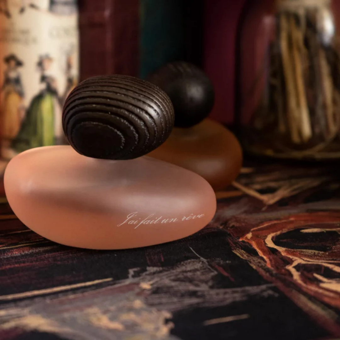 Majda Bekkali J’ai fait un rêve Clair Extrait de Parfum, roséfarbener Flakon auf dunkler Holzoberfläche inszeniert, warm und künstlerisch, erhältlich bei scent amor.