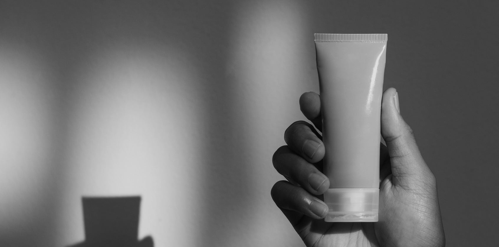 Eine Tube eines Pflegeprodukts wird vor einer weißen Wand in der Hand gehalten.