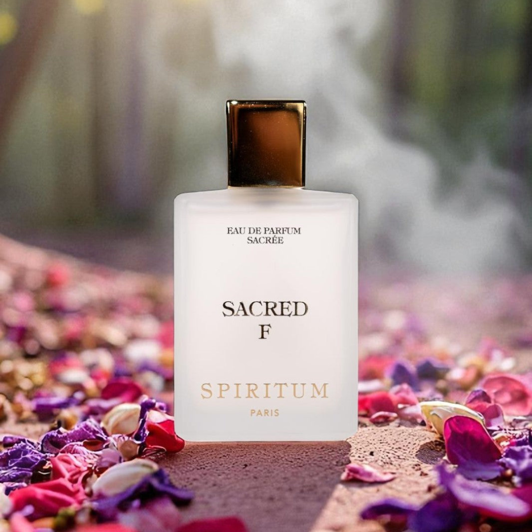 Spiritum Paris Sacred F Eau de Parfum, Flakon auf einem Bett aus bunten Blütenblättern im weichen Licht, sinnlich-mystischer Duftmoment, erhältlich bei scent amor
